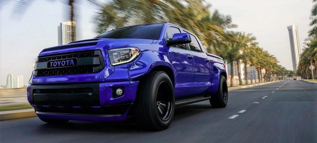 Front shot of blue Toyota Tundra traveling down a road lined with palm trees.
