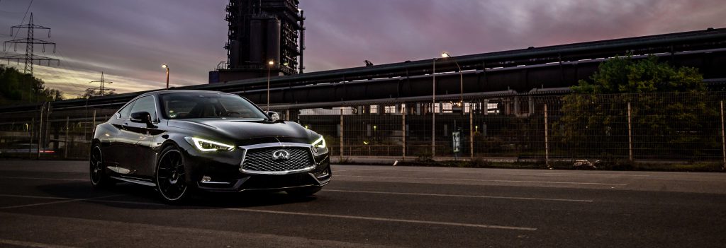 Night shot of Infiniti Q60 parked on the side of the road with headlights on.