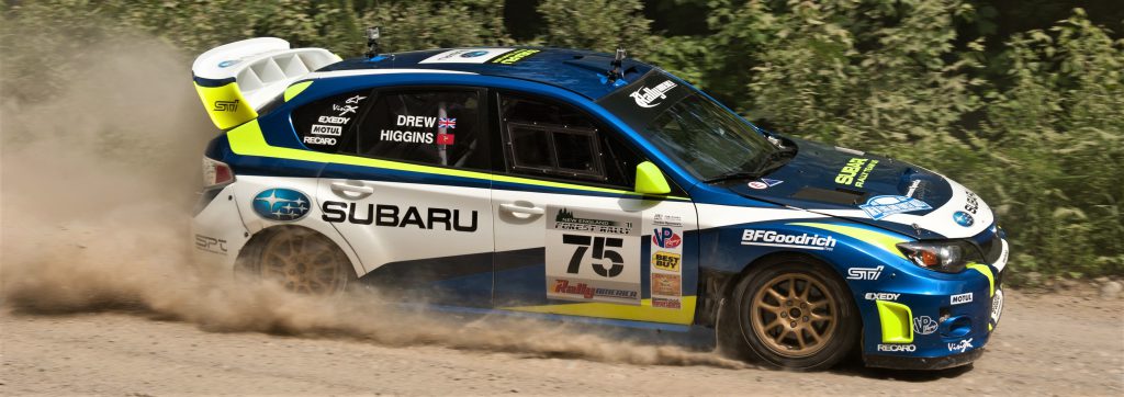 Subaru WRX STI at rally traveling on dirt path sporting decals from sponsors.